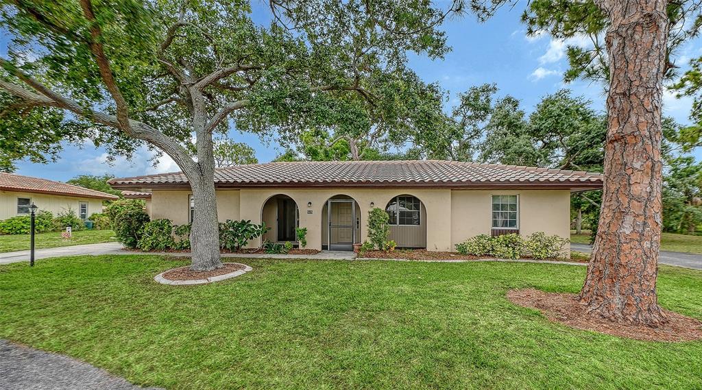 A single-story house with a tiled roof, arched entryways, and large trees in the yard — 515 ROUSSEAU DRIVE, NOKOMIS, FL