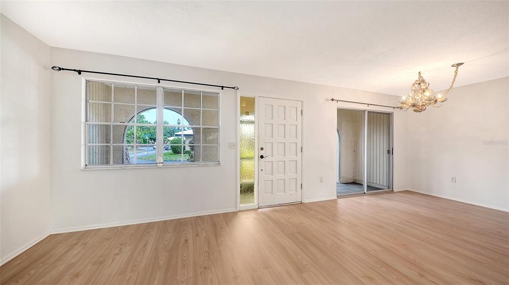 An empty living room features light wood-look flooring, a white front door, and a chandelier — 515 ROUSSEAU DRIVE, NOKOMIS, FL