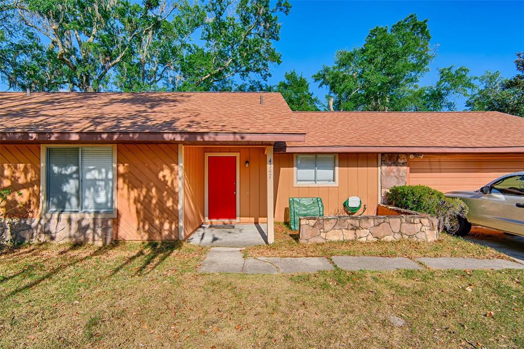 A single-story house with orange vertical siding, a red front door, and a stone planter — 4347 NW 43RD TERRACE, GAINESVILLE, FL