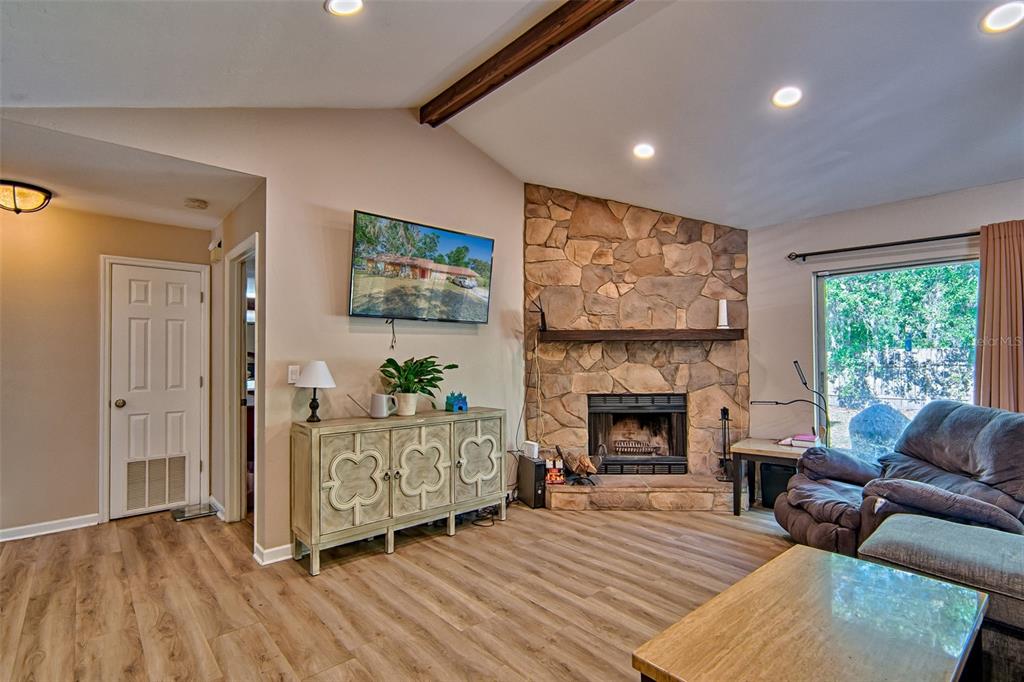 A living room features a stone fireplace, wood-look flooring, a television, and a console table — 4347 NW 43RD TERRACE, GAINESVILLE, FL