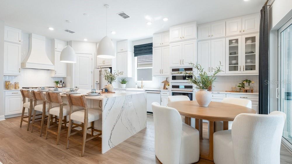 A bright kitchen features white cabinetry, a marble waterfall island, and a wooden dining table — 10606 ECLIPSE STREET, SARASOTA, FL