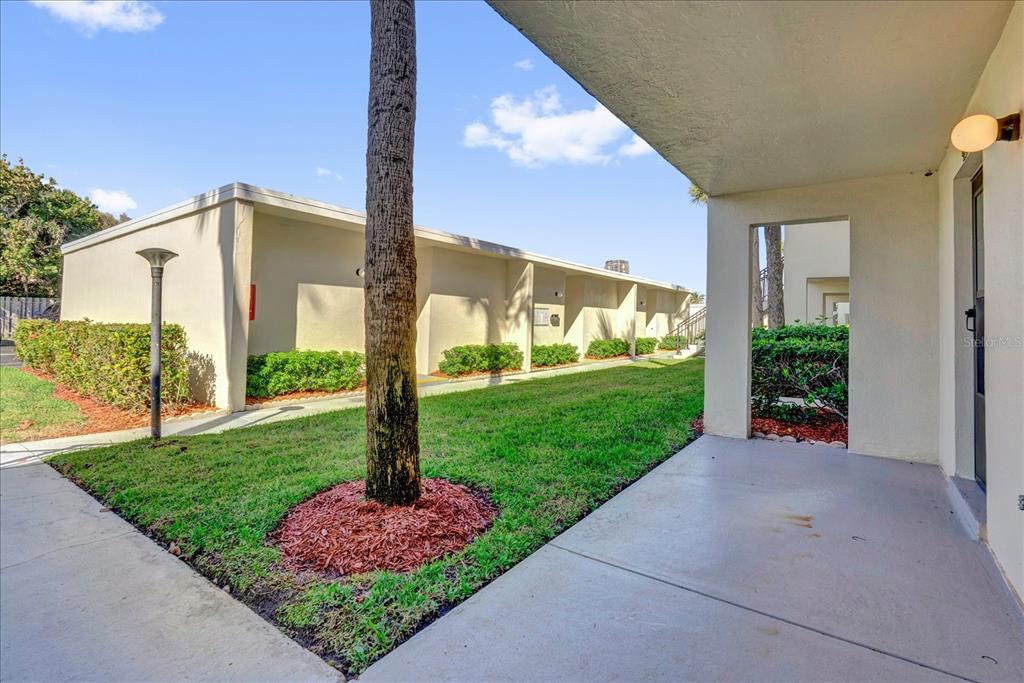 A concrete patio overlooks a grassy courtyard with a palm tree and apartment buildings — 2150 ATLANTIC STREET UNIT 413, MELBOURNE BEACH, FL