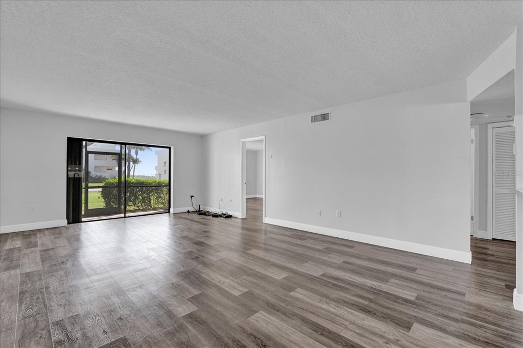 An empty living room with gray wood-look flooring, white walls, and a sliding glass door — 2150 ATLANTIC STREET UNIT 413, MELBOURNE BEACH, FL