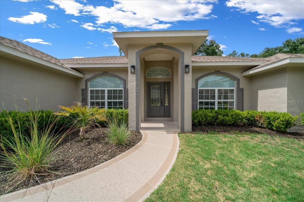 A beige house exterior features a covered entryway, arched windows, and a curved concrete walkway — 5413 SE 107TH STREET, BELLEVIEW, FL
