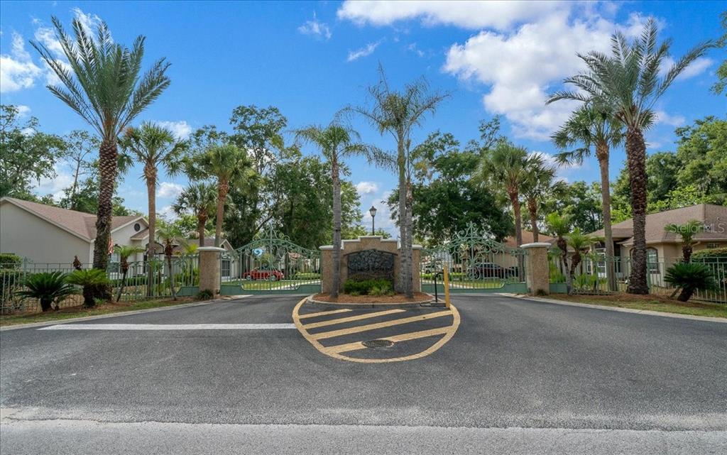 A gated entrance with palm trees and a paved driveway leading into a residential community — 5413 SE 107TH STREET, BELLEVIEW, FL