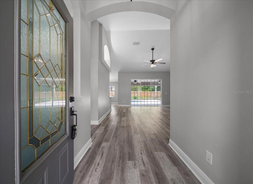 An entryway leads into a living area with gray wood-look flooring and a glass door — 5413 SE 107TH STREET, BELLEVIEW, FL
