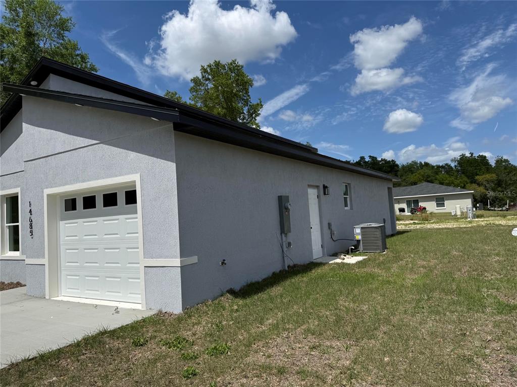 A side view of a gray stucco house with a white garage door and yard — 14685 SW 22 PLACE, OCALA, FL