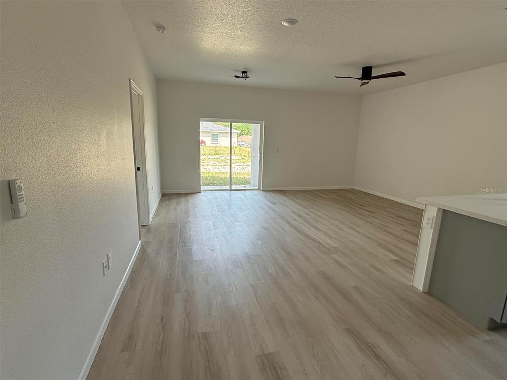 An open-concept living area features light wood-look flooring, a ceiling fan, and sliding glass doors — 14685 SW 22 PLACE, OCALA, FL