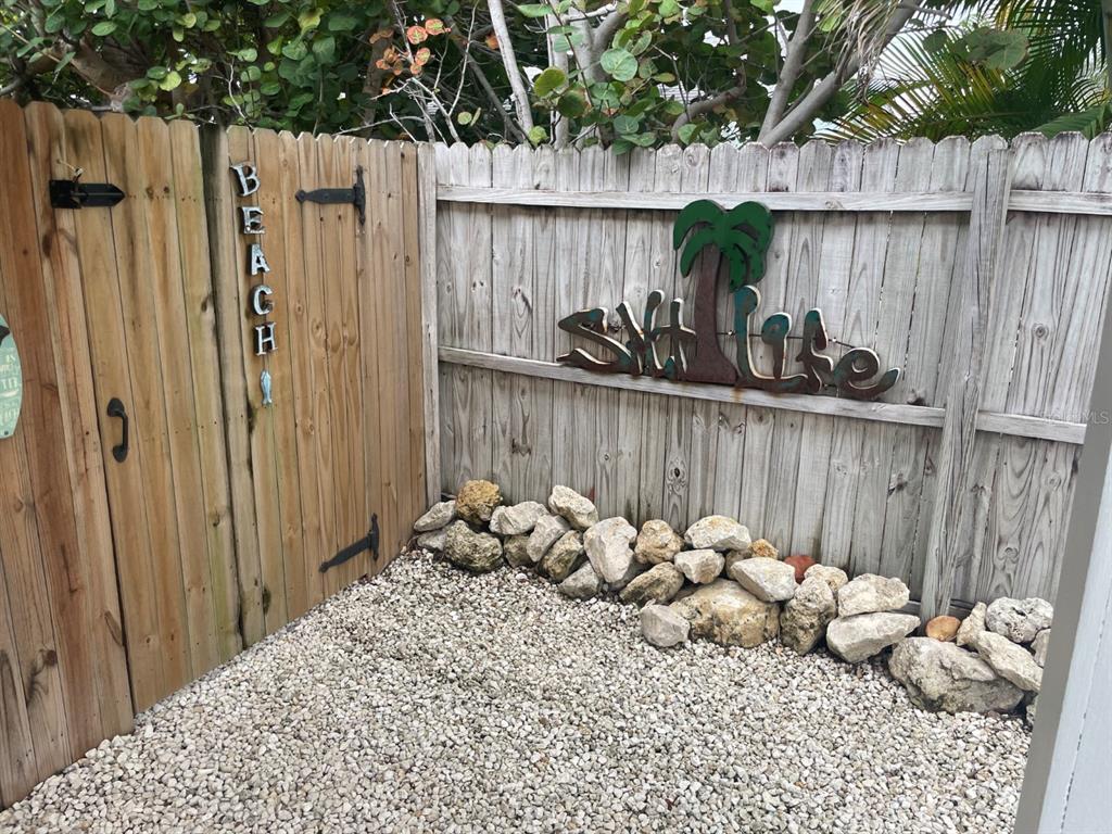 A wooden fence with a gate, decorative signs, and a gravel ground area with rocks — 720 E GULF BOULEVARD UNIT B, INDIAN ROCKS BEACH, FL