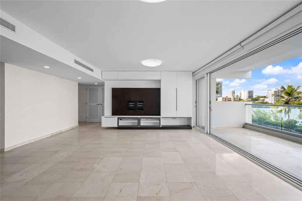 A minimalist living room features large light-colored floor tiles, a built-in media wall, and a balcony — #6 MARIANO RAMÍREZ BAGES UNIT 1, SAN JUAN, PR