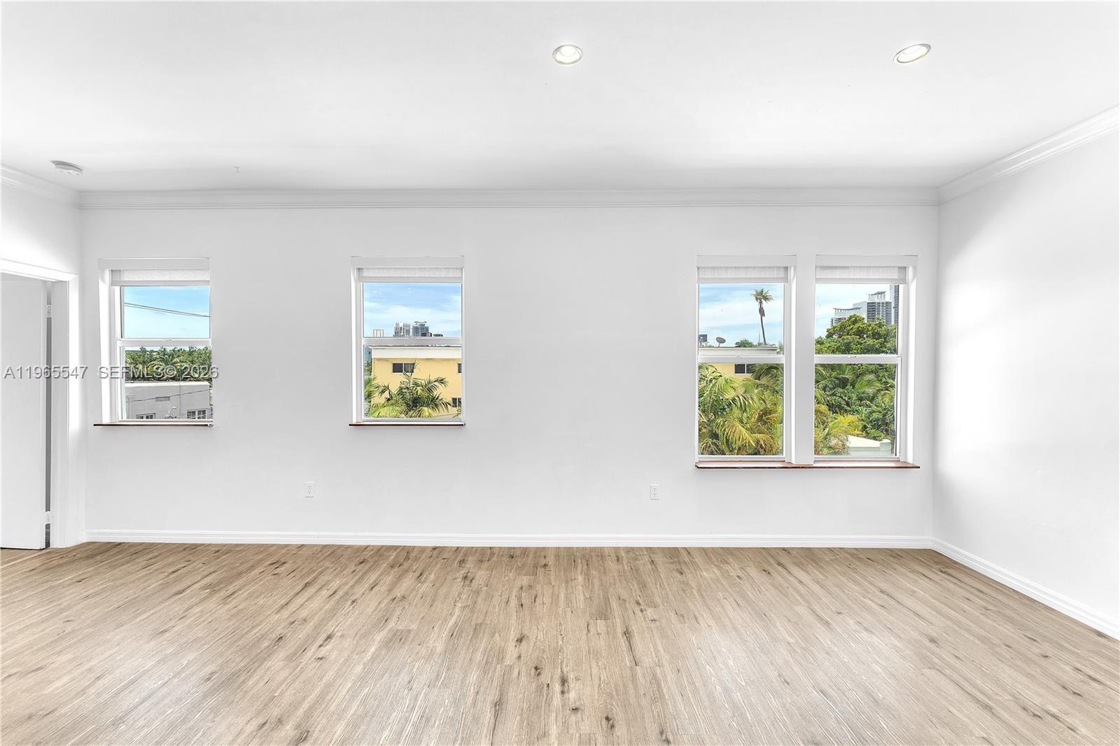 An empty room features white walls, light wood-look flooring, and four windows overlooking trees — 737 Jefferson Ave # 305, Miami Beach FL 33139, MIAMI BEACH, FL