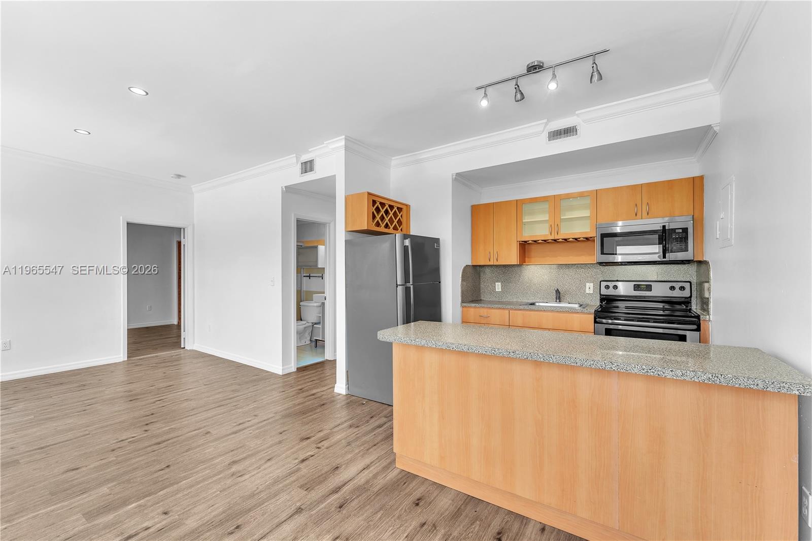 A kitchen with light wood cabinets and a granite breakfast bar opens to a living area — 737 Jefferson Ave # 305, Miami Beach FL 33139, MIAMI BEACH, FL