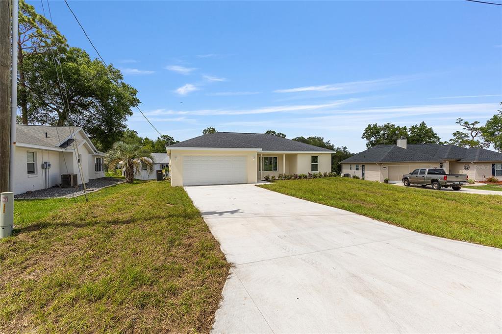 A single-story house with a white garage and concrete driveway sits on a grassy lot — 62 MALAUKA RADIAL, OCKLAWAHA, FL