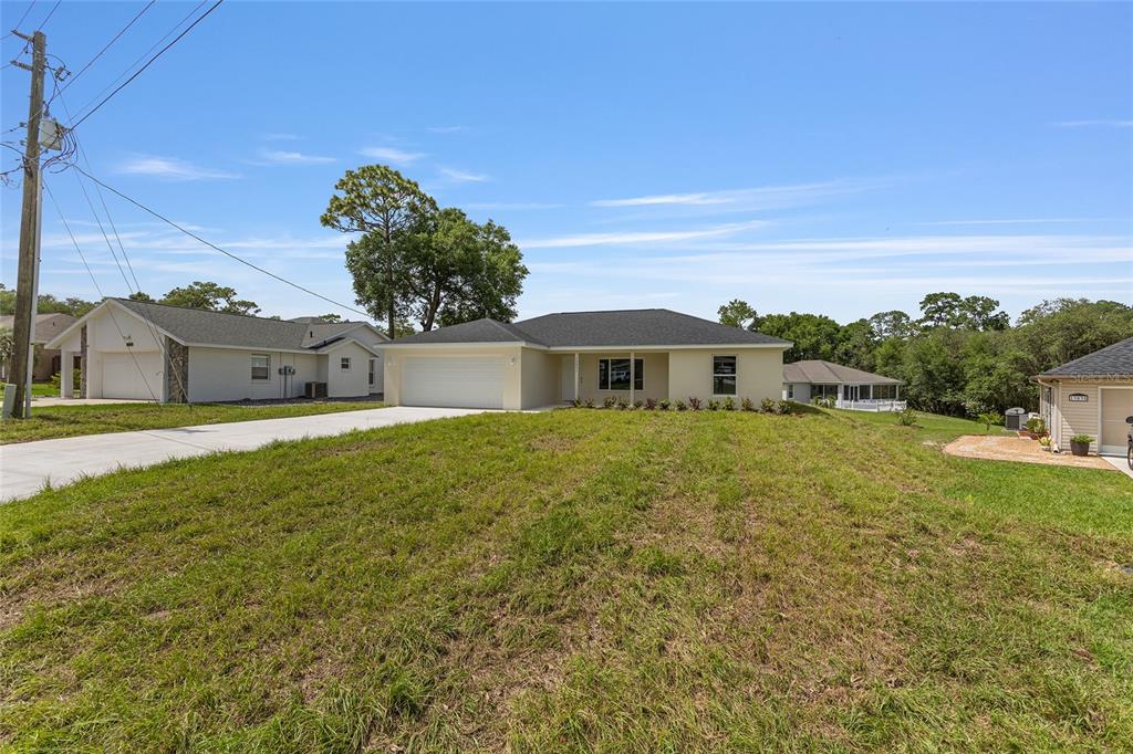 A single-story house with a white garage and light-colored exterior sits on a grassy lot — 62 MALAUKA RADIAL, OCKLAWAHA, FL