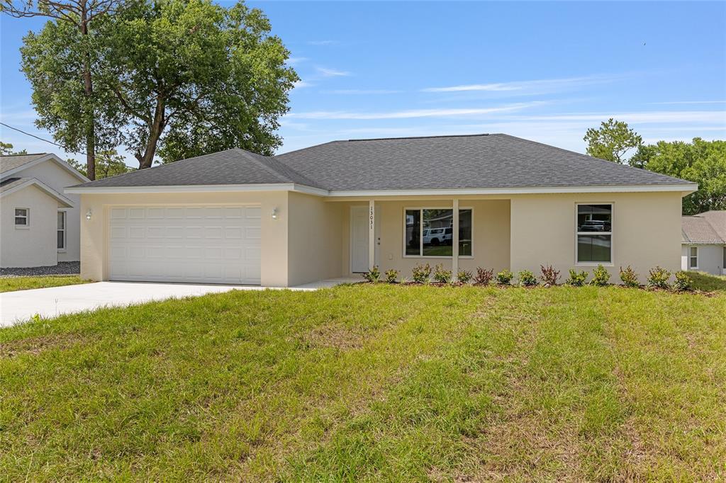 A single-story house with a beige stucco exterior, a two-car garage, and a shingled roof — 62 MALAUKA RADIAL, OCKLAWAHA, FL