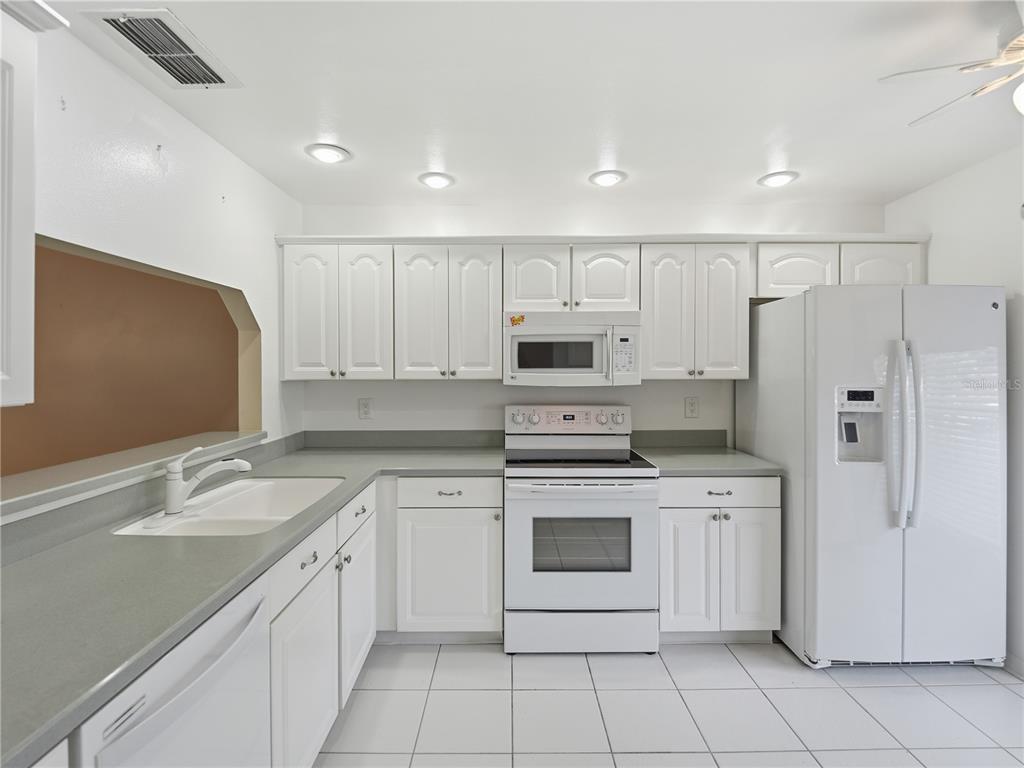 A white kitchen features gray countertops, white cabinetry, and white appliances on a tiled floor — 914 MICHIGAN AVENUE, ST CLOUD, FL