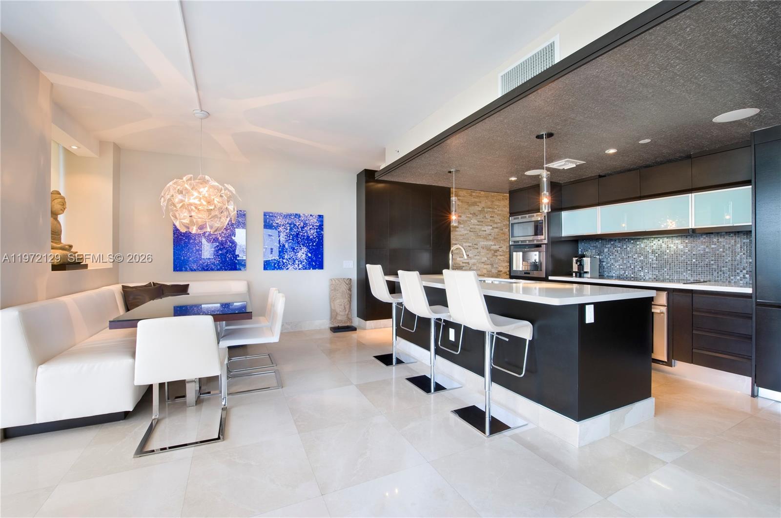 A modern kitchen and dining area features dark cabinetry, a white island, and white seating — 5875 Collins Ave # 1008, Miami Beach FL 33140, MIAMI BEACH, FL