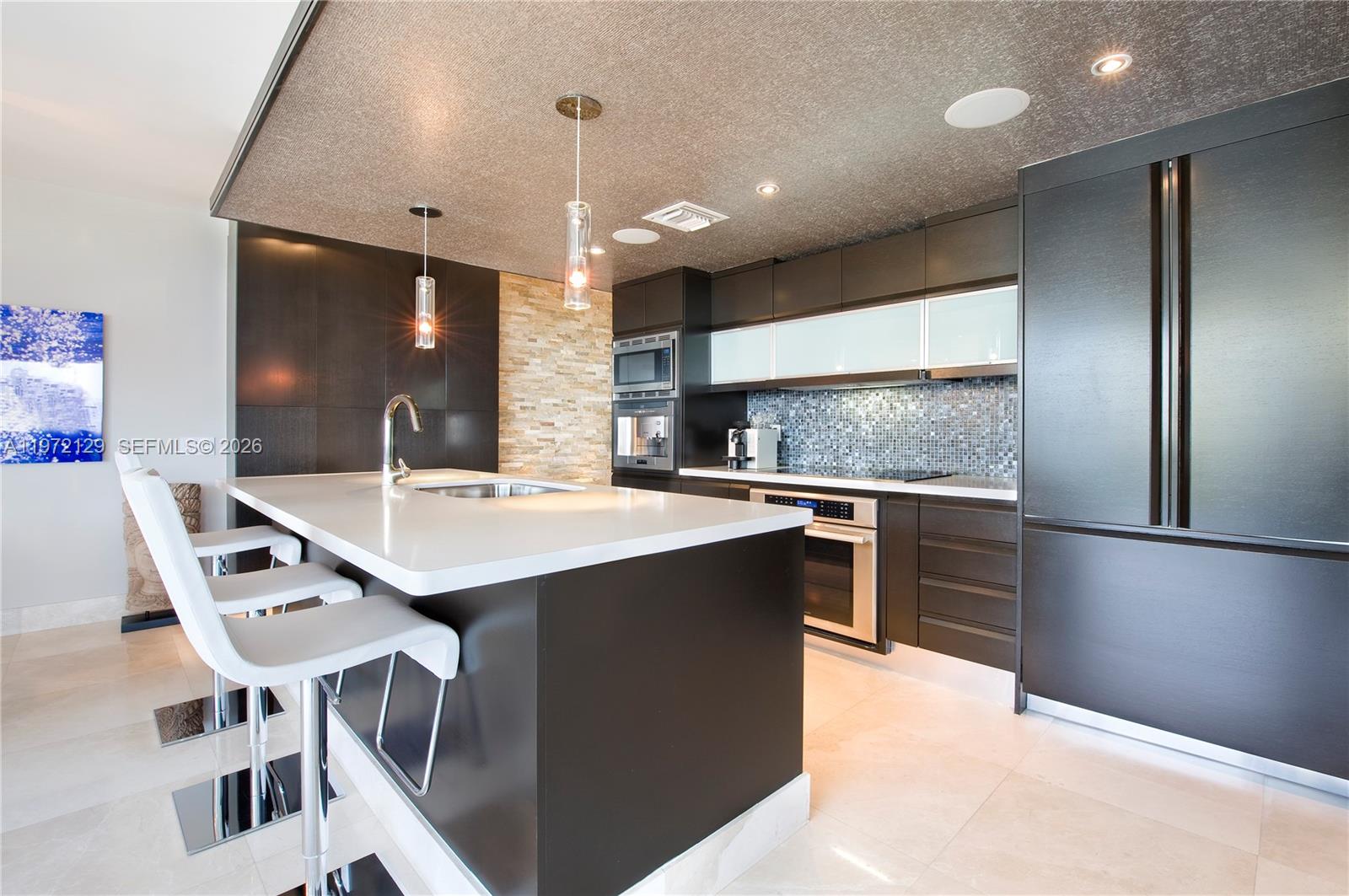 A modern kitchen features dark cabinetry, a white island countertop, and a textured ceiling — 5875 Collins Ave # 1008, Miami Beach FL 33140, MIAMI BEACH, FL