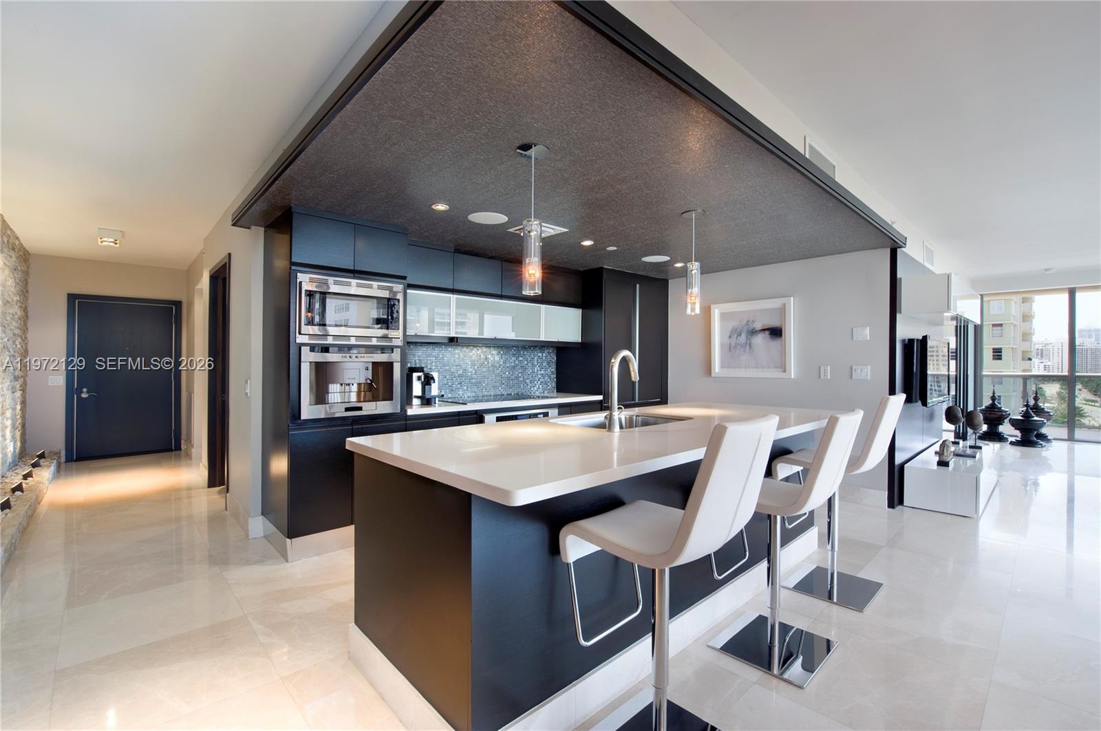 A modern kitchen features dark cabinetry, a white island with bar stools, and a textured ceiling — 5875 Collins Ave # 1008, Miami Beach FL 33140, MIAMI BEACH, FL