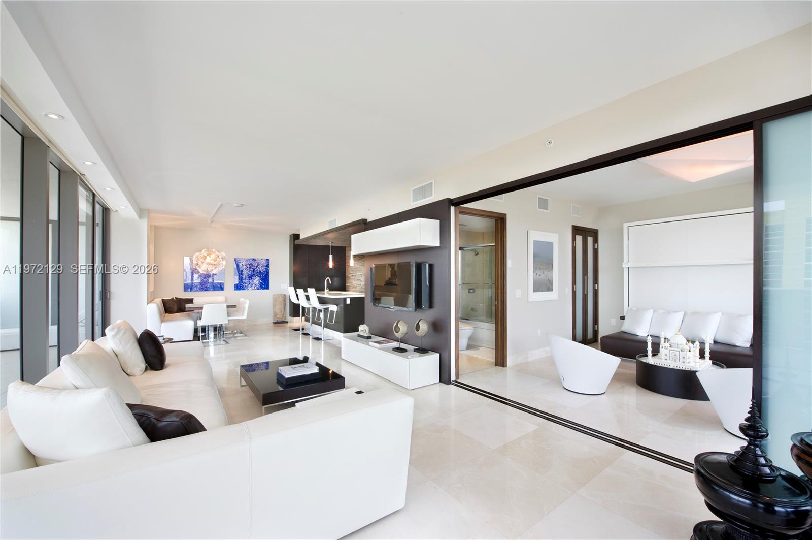 A modern open-concept living area features white tile floors, a kitchen island, and sliding doors — 5875 Collins Ave # 1008, Miami Beach FL 33140, MIAMI BEACH, FL