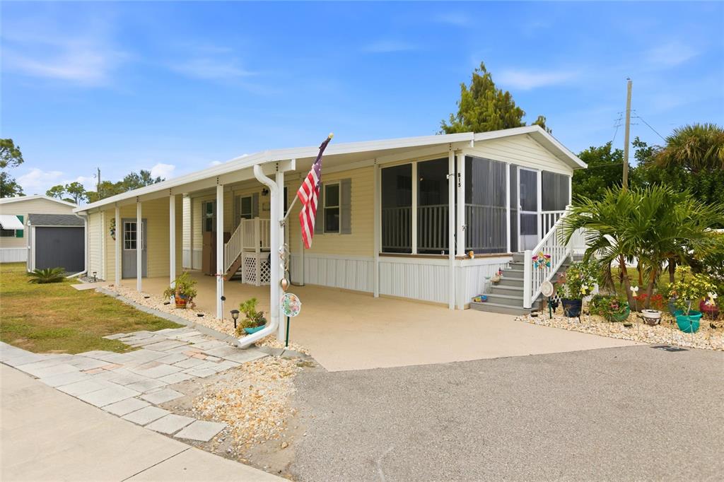 A light yellow mobile home features a covered carport, a screened-in porch, and an American flag — 15 N CARDINAL UNIT B15, PUNTA GORDA, FL