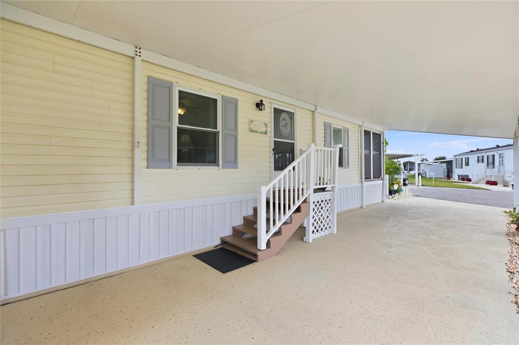 A yellow mobile home exterior features a covered carport, stairs with railings, and gray shutters — 15 N CARDINAL UNIT B15, PUNTA GORDA, FL