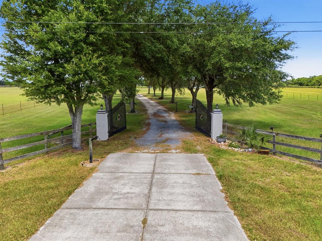 A concrete driveway leads to an open gate flanked by trees and wooden fencing — 11748 NE JACKSONVILLE ROAD, ANTHONY, FL