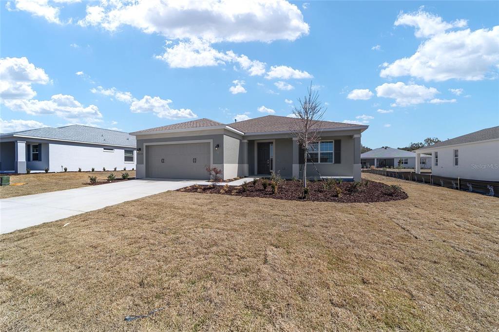 A single-story house with a two-car garage and a front yard under a blue sky — 10339 SW 105TH TERRACE, OCALA, FL