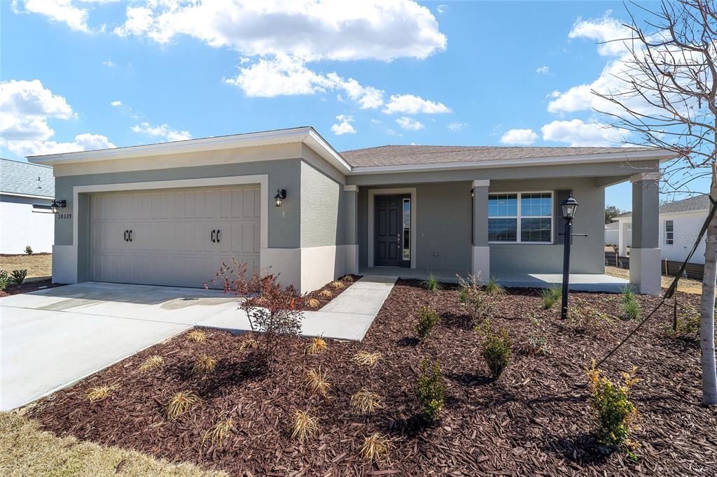 A single-story house with a two-car garage, gray stucco exterior, and a covered front porch — 10339 SW 105TH TERRACE, OCALA, FL