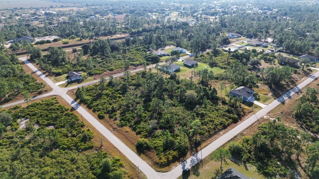 An aerial view shows a vacant, wooded residential lot situated at a paved road intersection — 4400 E 5TH STREET, LEHIGH ACRES, FL
