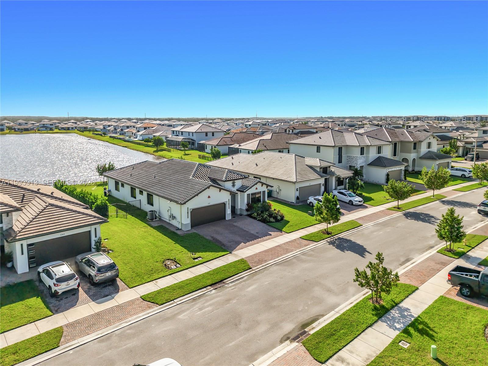 An aerial view shows a suburban street with houses, a lake, and parked cars — 5246 Karlia Drive, Ave Maria FL 34142, AVE MARIA, FL