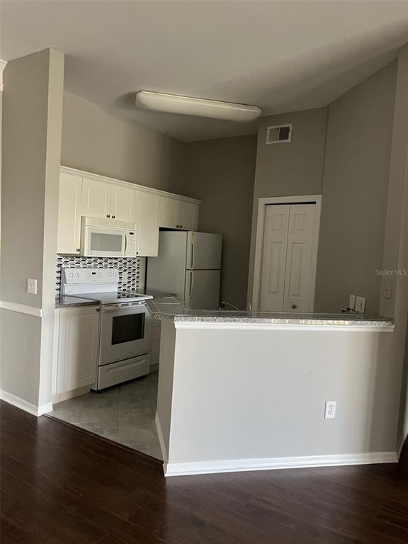 A kitchen features white cabinets, a white stove, a refrigerator, and a granite breakfast bar — 5134 NORTHRIDGE ROAD UNIT 302, SARASOTA, FL