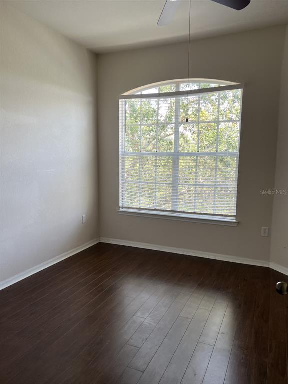An empty room with dark wood flooring, beige walls, and an arched window with blinds — 5134 NORTHRIDGE ROAD UNIT 302, SARASOTA, FL