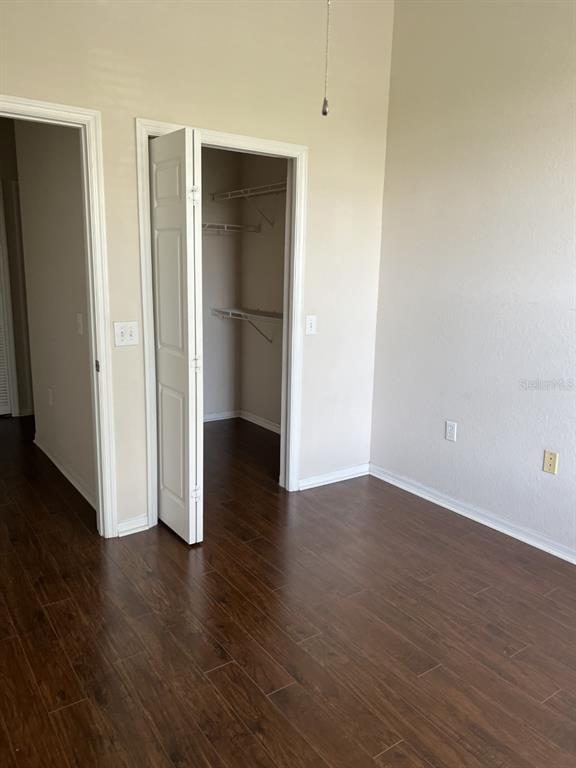 A room with dark wood-look flooring, beige walls, and an open walk-in closet — 5134 NORTHRIDGE ROAD UNIT 302, SARASOTA, FL