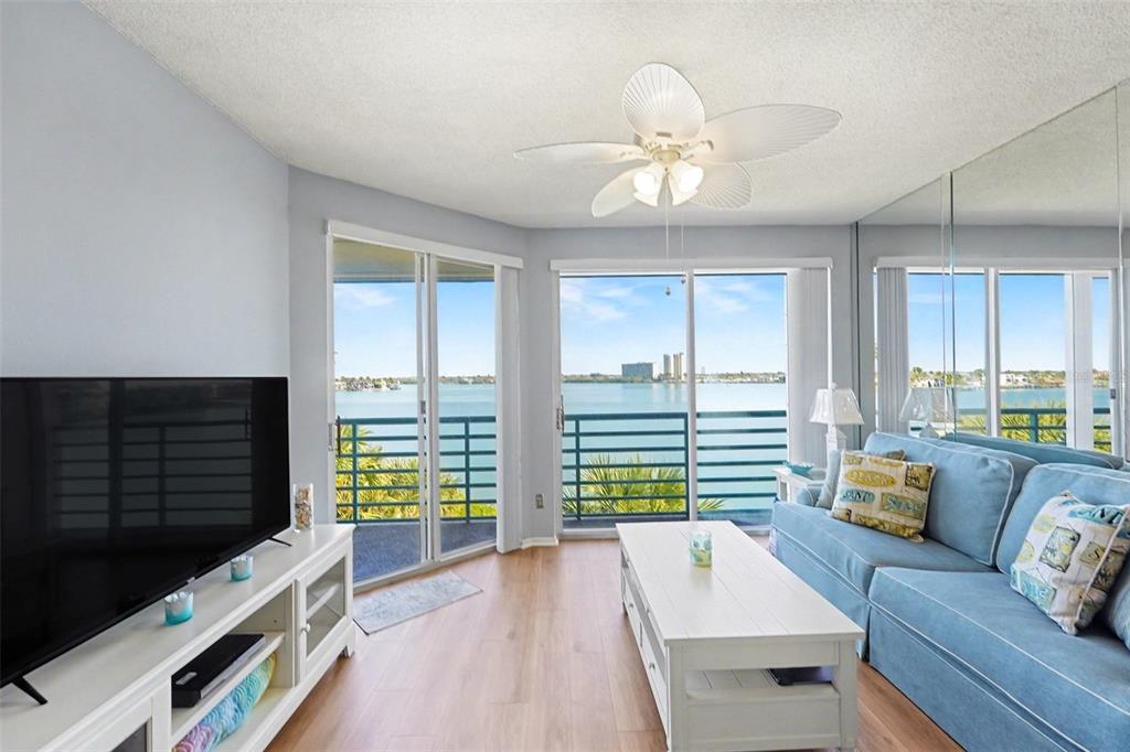 A living room features light wood flooring, a blue sofa, and sliding doors overlooking water — 8021 SAILBOAT KEY BOULEVARD S UNIT 304, ST PETE BEACH, FL
