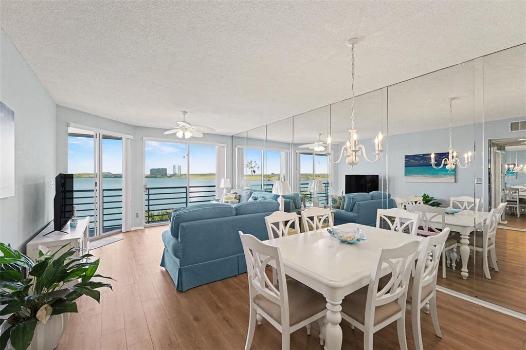 A dining area and living room with light wood floors, blue furniture, and mirrored walls — 8021 SAILBOAT KEY BOULEVARD S UNIT 304, ST PETE BEACH, FL