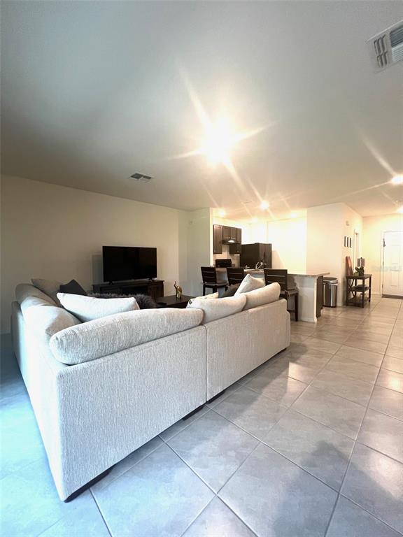 A living room with a large sectional sofa faces a television near an open kitchen — 9033 ALBA LANE, KISSIMMEE, FL