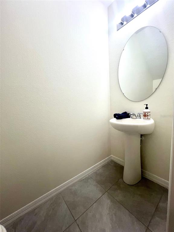 A small bathroom features a pedestal sink, an oval mirror, and gray tile flooring — 9033 ALBA LANE, KISSIMMEE, FL