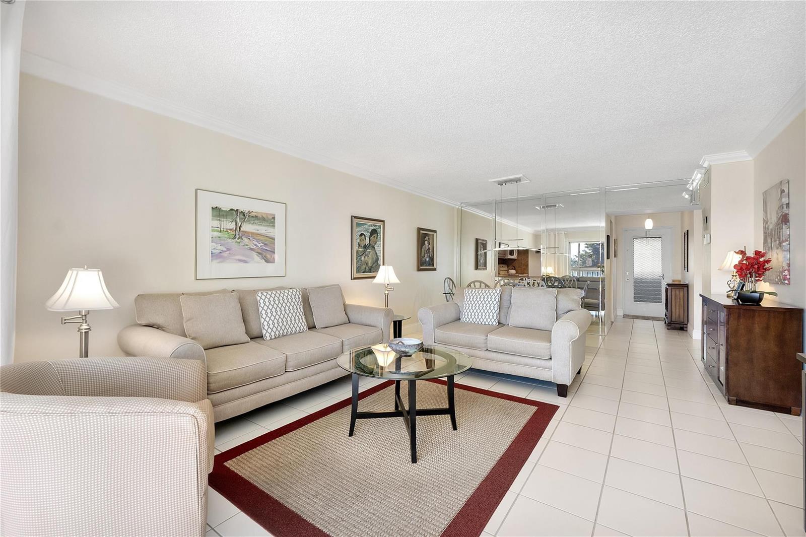 A living room features beige sofas, a glass coffee table, tile flooring, and mirrored walls — 7787 Golf Circle Drive # 312, Margate FL 33063, MARGATE, FL