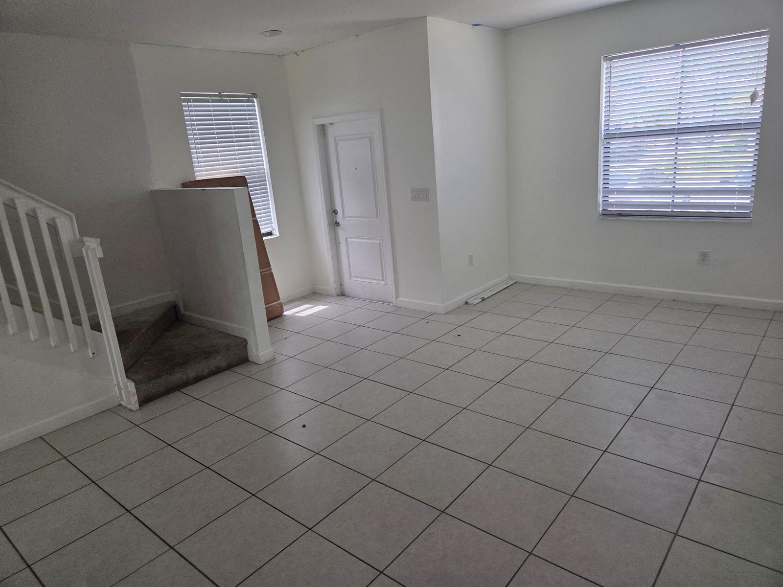An empty room with white walls, tiled floors, a staircase, and two windows with blinds — 23317 SW 129th Path, Homestead FL 33032, HOMESTEAD, FL