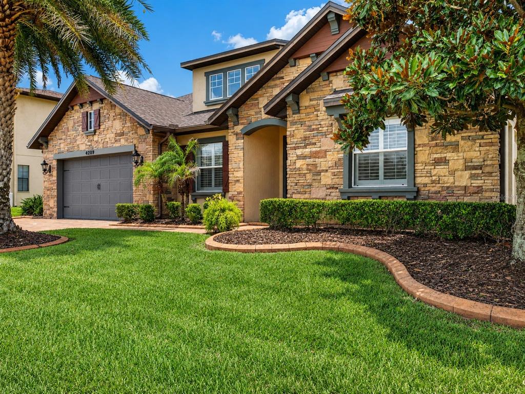 A single-story house with a stone facade, a two-car garage, and a landscaped front yard — 4209 FOXHOUND DRIVE, CLERMONT, FL