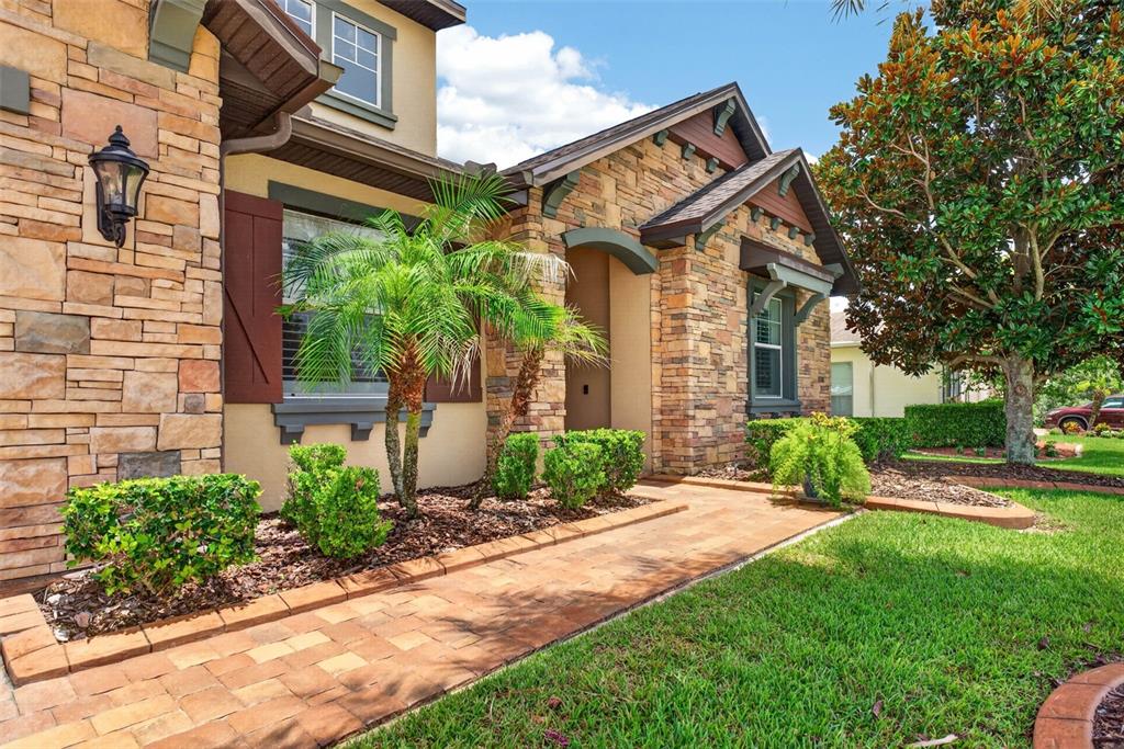 A stone-facade house exterior features a brick walkway, manicured shrubs, and a palm tree — 4209 FOXHOUND DRIVE, CLERMONT, FL