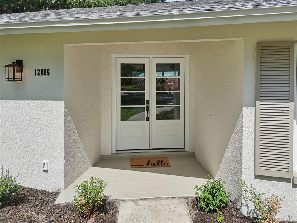 A white double front door with glass panels sits under a covered entryway — 12805 KIMBERLY OAKS CIRCLE, LARGO, FL