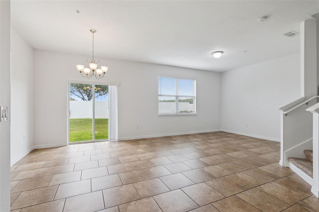 An open living area features tan tile flooring, a chandelier, a sliding glass door, and stairs — 6558 S GOLDENROD ROAD UNIT 78B, ORLANDO, FL