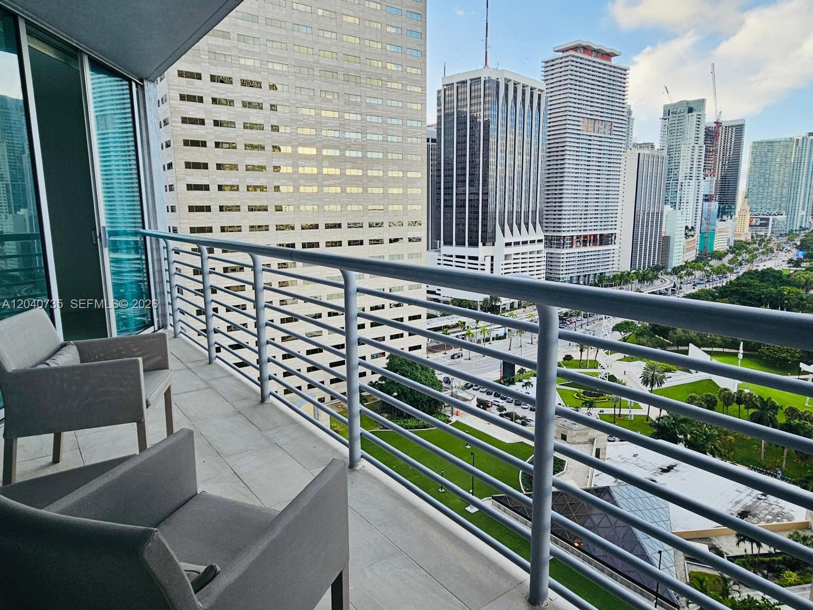 A balcony with two gray chairs overlooks a city skyline and a green park — 335 S Biscayne Blvd # 2202, Miami FL 33131, MIAMI, FL