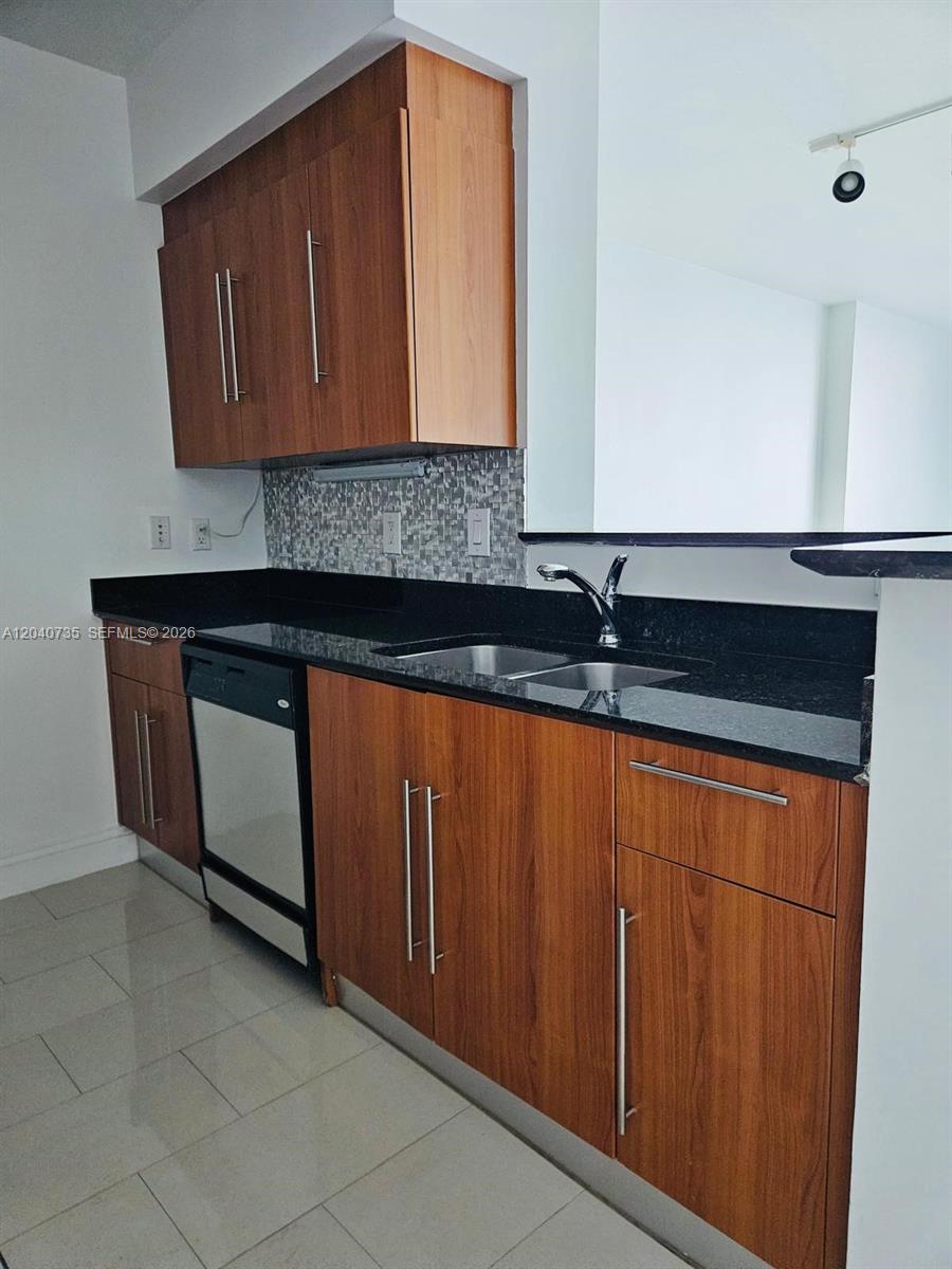 A kitchen features wood-grain cabinets, black countertops, a stainless steel dishwasher, and tiled flooring — 335 S Biscayne Blvd # 2202, Miami FL 33131, MIAMI, FL