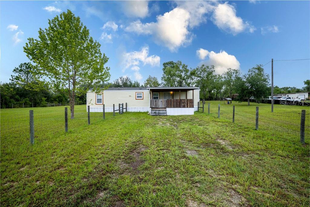 A single-story manufactured home with a front porch sits on a large, fenced grassy lot — 12551 NE 14TH STREET, WILLISTON, FL