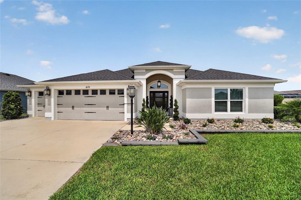 A single-story house with a beige stucco exterior, a three-car garage, and a landscaped yard — 6172 DANIELSON LOOP, THE VILLAGES, FL