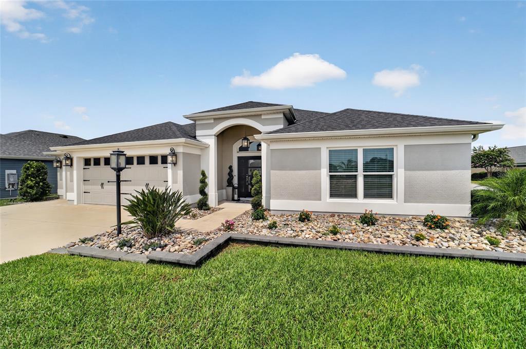 A single-story house with a beige stucco exterior, a two-car garage, and a rock garden — 6172 DANIELSON LOOP, THE VILLAGES, FL