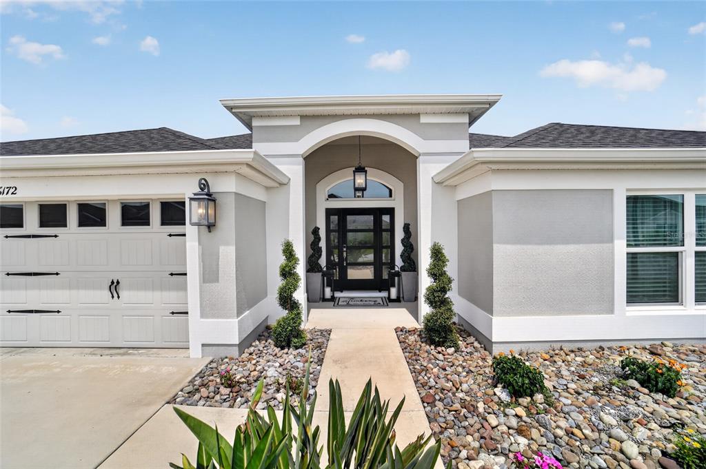 The exterior of a single-story house features a gray stucco facade, a garage, and a walkway — 6172 DANIELSON LOOP, THE VILLAGES, FL